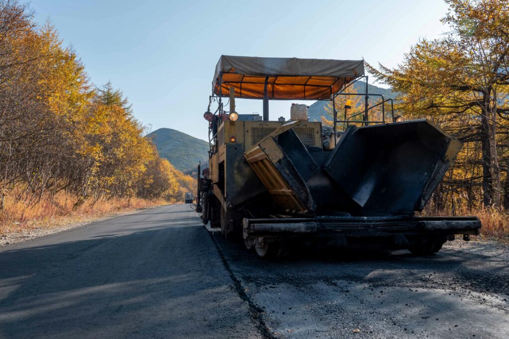 Road paving machine on a scenic autumn highway surrounded by colorful trees.
